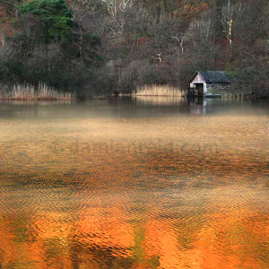 Mist sliding over Rydal Water lake as sun begins to set in winter; boathouse and trees in background