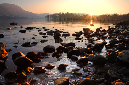 Sunset over Ullswater in Winter with rocks and ice in foreground, near marina, Watermillock, Lake District