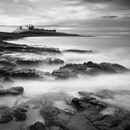 Dunstanburgh Castle in late afternoon light at high tide with waves spilling on rocks on Craster side, Northumberland