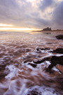 Sunrise at Bamburgh Beach, Northumberland with dawn light on waves and Bamburgh Castle in background